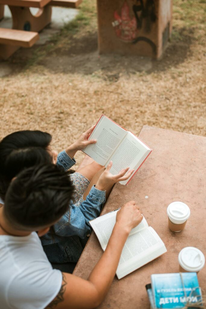 Couple enjoying a quiet reading session outdoors with coffee on a picnic table.